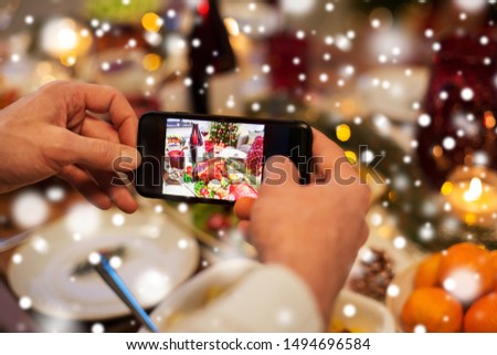 food, technology and holidays concept - close up of male hands photographing roast turkey by smartphone at christmas dinner over snow