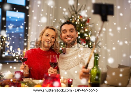 christmas, holidays, technology and people concept - happy couple in taking picture by selfie stick at home dinner over snow