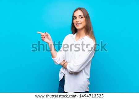 Young woman over isolated blue background pointing finger to the side