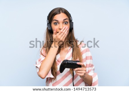 Young woman playing with a video game controller over isolated blue wall with surprise facial expression