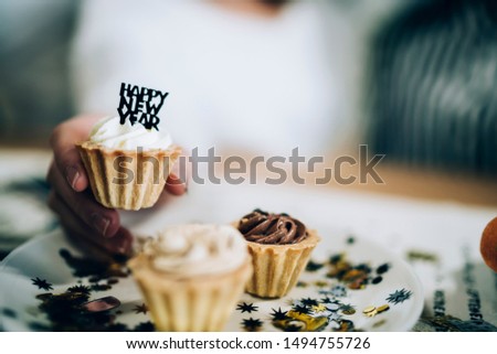 Crop young women in casual clothes taking sweet dessert with topper from festive plate with glitter while sitting by table
