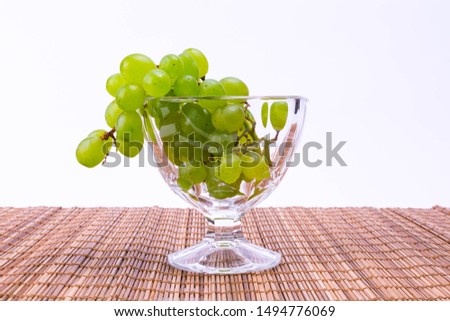a sprig of ripe green grapes with drops on the surface lies in a glass, closeup photo