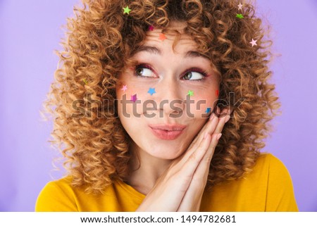 Image closeup of cute pretty curly girl smiling and dreaming with multicolored glitter stars on her face isolated over violet background