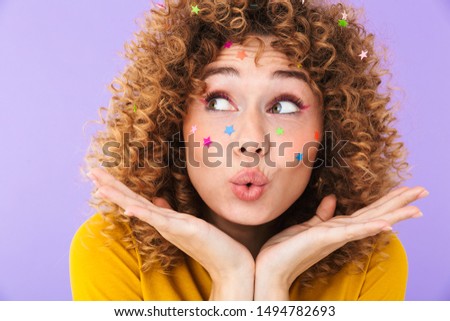 Image closeup of caucasian pretty curly girl having fun and rejoicing with multicolored glitter stars on her face isolated over violet background