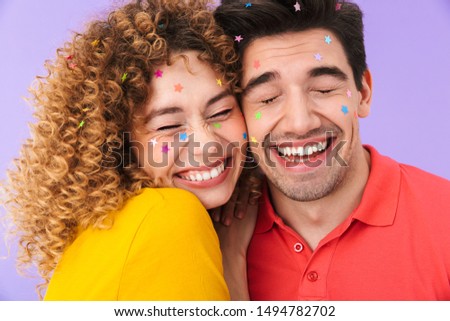 Image of optimistic content couple laughing and hugging while having party with glitter stars on faces isolated over violet background