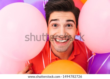 Image closeup of happy delighted man rejoicing while posing in multicolored air balloons isolated over violet background