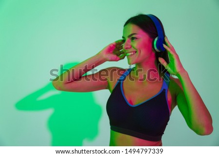 Image of happy smiling optimistic young strong fitness woman isolated with led flash lights listening music with headphones.