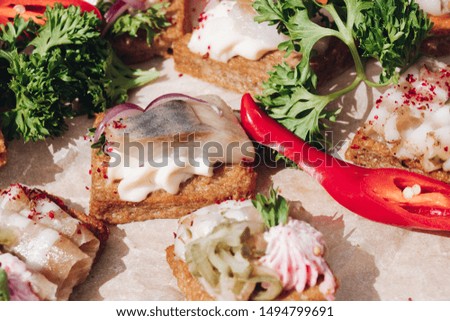 Close-up of tasty crispy sandwiches or canapes with cream cheese, onion and herring on the top. Parsley and chilli pepper on the platter.