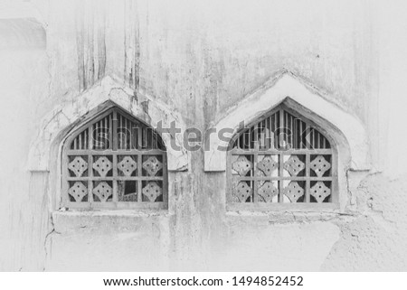 A monochrome, filtered and vignetted image of two ogee arched windows with wooden lattices in the wall of an abandoned, derelict building in the Middle East.