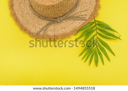 Straw hat with fresh green bamboo leaves with tiny branch and fine or tapering leaves on isolated yellow background
