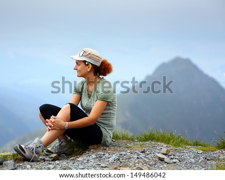 Caucasian woman with cap sitting on a mountain with a peak in background