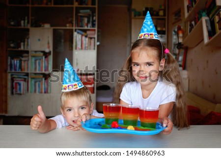 Happy sister and brother having fun at birthday party, glass with traffic light colored jelly, holiday and celebration concept. Indoor portrait, focus on girl