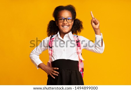 Great Idea. Nerdy African American Schoolgirl Pointing Finger Up Having Question On Yellow Studio Background.