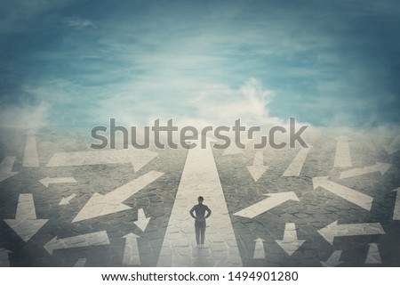 Doubtful person, hands on hips, choosing the way as multiple arrows on the road showing a mess of different directions. Choosing the correct pathway, difficult decision concept, confusion symbol. Royalty-Free Stock Photo #1494901280