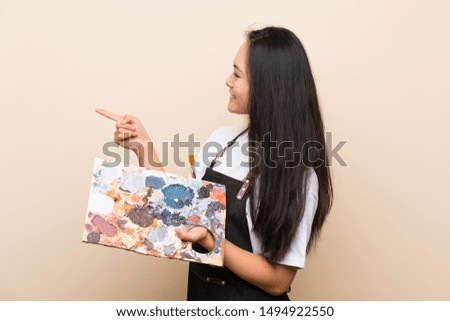 Teenager painter asian girl pointing to the side to present a product