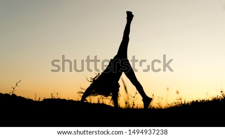 Silhouette of small girl running and jumping on top of the hill during sunset
