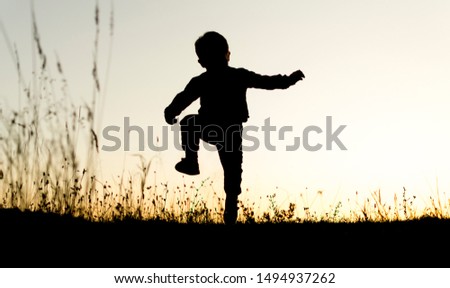 Silhouette of small boy running on top of the hill in sunset