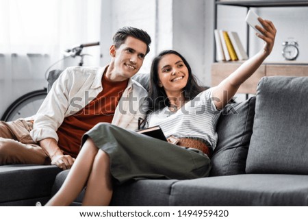 happy multicultural students smiling and taking selfie in apartment 