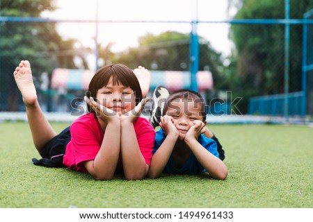 Picture of brother and sister having fun in the park, two cheerful children laying down on green grass, little girl and boy playing outdoors