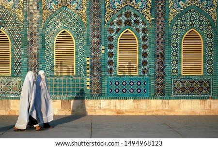 The Blue Mosque in Mazar-i-Sharif, Balkh Province in Afghanistan. Two women wearing white burqas (burkas) walk past a wall of the mosque adorned with colorful tiles and mosaics. Northern Afghanistan. Royalty-Free Stock Photo #1494968123