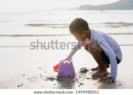 Asian boy playing bucket toy and making sand castle on the sand beach at the sea side.Happy time on travel vacation day.Vintage style.