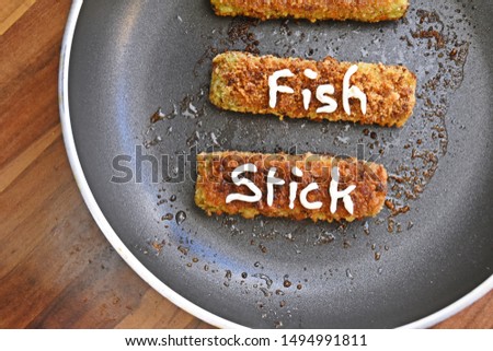 Picture from the top of a pan with fried fish fingers with spinach on a dark wooden surface - Delicious freshly fried dark fish sticks in a black teflon pan