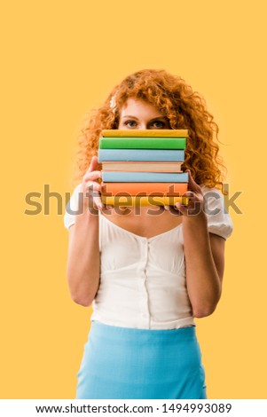 beautiful redhead student holding books isolated on yellow 