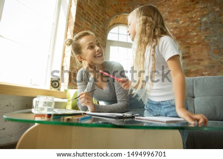 Female caucasian teacher and little girl, or mom and daughter. Homeschooling. Sitting on the sofa and drawing with paints, writing, talking and having fun. Education, school, studying concept.