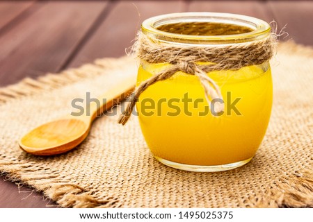 Pure or desi ghee (ghi), clarified melted butter. Healthy fats bulletproof diet concept or paleo style plan. Glass jar, wooden spoon on vintage sackcloth. Wooden boards background, close up Royalty-Free Stock Photo #1495025375