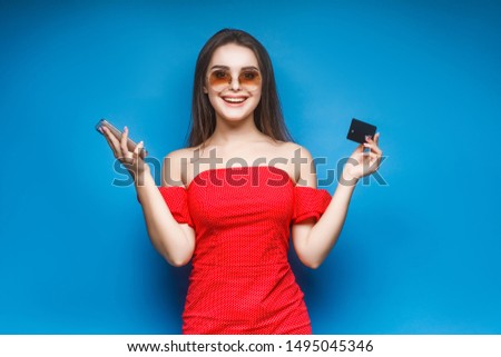 Picture of a cheerful young brunette woman in red summer dress holding credit card, online shopping concept.