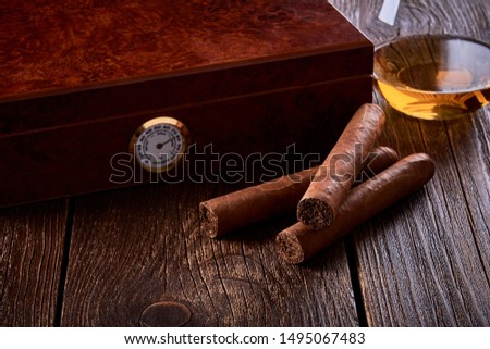 Still life with wooden box for humidification, three cigars and glass of whiskey on old table. Royalty-Free Stock Photo #1495067483
