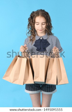Child with a packet isolated on blue background. Holiday present, shopping. Kid happy shopping in mall. Happy girl with long curly hair. High resolution photo. Full depth of field.