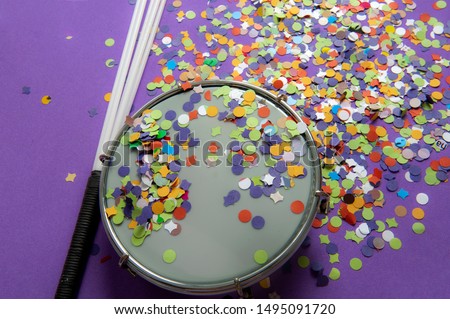 Chopped colorful confetti on tambourine used in the Brazilian Carnival. Popular party of samba. Instrument used in street block, samba school parade. Purple background. From above.Space for your text. Royalty-Free Stock Photo #1495091720