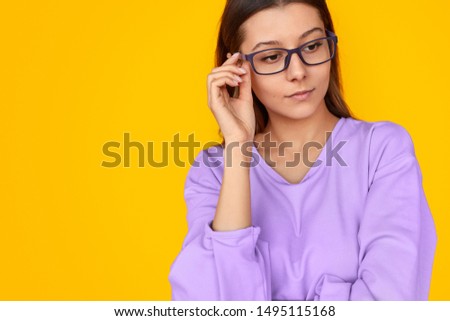 Stylish pensive young woman in eyeglasses and colourful shirt looking away over yellow background