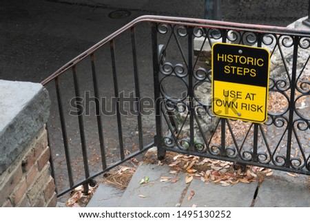 Yellow and black Historic steps use at own risk sign on wrought iron railing of brick and stone stairs in Savannah Georgia
