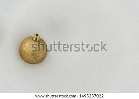 A sparkling golden Christmas ball lies in the winter white snow. There is a place for text. Christmas concept.