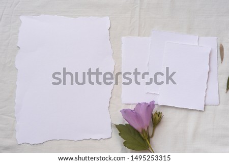 Blank white greeting card with flower on textile white background. Top view. Mock up