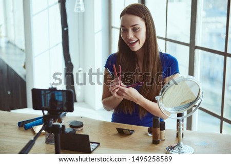 Young beautiful woman blogger using cosmetics while shooting at camera at home