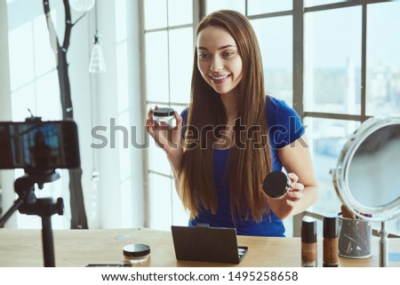 Young beautiful woman blogger using cosmetics while shooting at camera at home