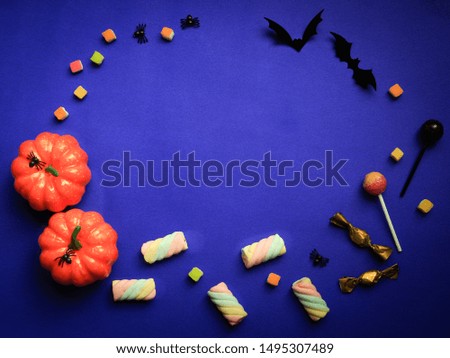 Halloween decorations concept background, top view of orange pumpkin, sweet candy snack, spider and black bat on purple background with copy space.
