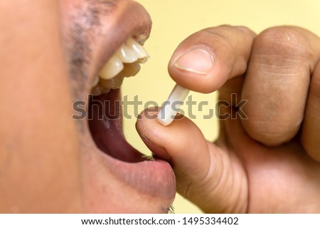 A male patient is taking a white pill in his mouth to cure his illness.