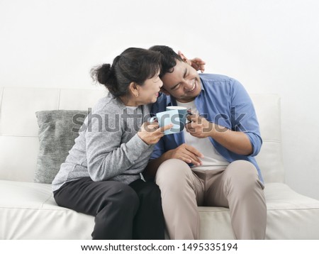 Asian mother and her son talking and drinking at home, lifestyle concept.