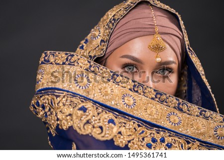 Close up portrait of a beautiful female model wearing Indian costume with hijab isolated over dark background. Studio fashion and beauty make up concept.