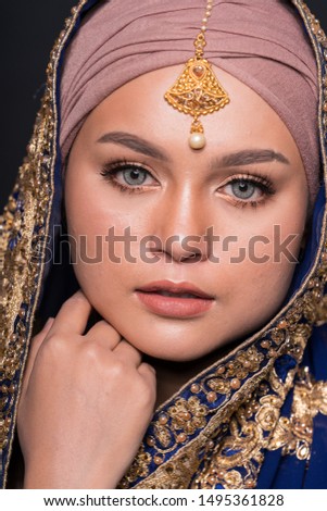 Close up portrait of a beautiful female model wearing Indian costume with hijab isolated over dark background. Studio fashion and beauty make up concept.