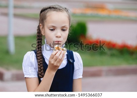 Girl teenager blonde with pigtails in a school uniform eats a bun.