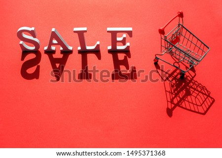 Small empty shopping trolley cart and word SALE of white letters casts a large shadow on red background with copy space. Concept black friday sale. Creative template for your text, design