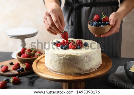 Woman decorating delicious homemade cake with fresh berries at table indoors, closeup Royalty-Free Stock Photo #1495398176