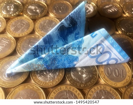 A banknote of 500 Kazakhstani tenge folded in the form of an airplane figurine lies on coins of 100 tenge. Background and texture. Close-up.
