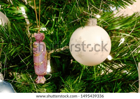 Nice bright pink candy Christmas toy and bright white toy ball with snowflake picture hanging on the green spruce branch and waiting for new year