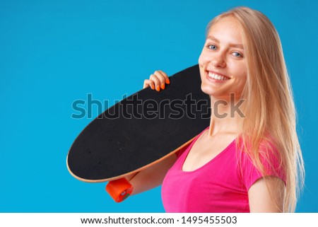 Attractive young woman holding her skateboard over blue background